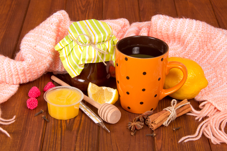 Cup of hot tea with lemon and honey from cold, a warm scarf on background of wooden tableの写真素材