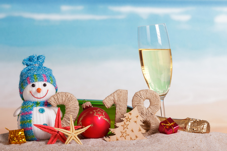 New Year inscription 2018, a bottle and a glass of champagne, snowman, gifts, Christmas ball and starfish in the sand on the beach.の写真素材