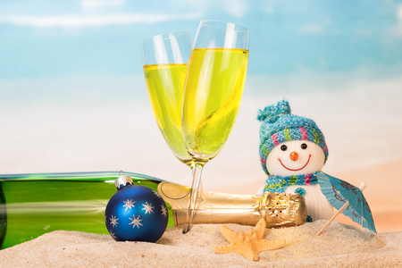 Bottle and two glasses with champagne, snowman, Christmas ball, umbrella, starfish in the sand against the sea.の写真素材