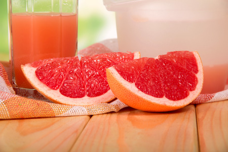 Pieces of grapefruit, a glass of juice and a napkin on a wooden tableの写真素材