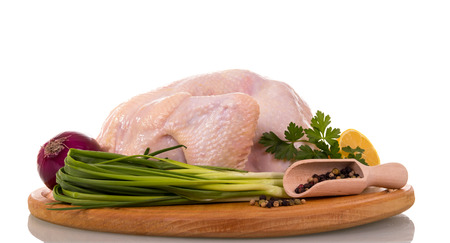 Blackboard with whole raw chicken carcass, scoop with pepper, onion, parsley and lemon portion isolated on white background.の写真素材