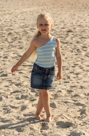 Charming blond girl in clothes walking along sandy beachの写真素材