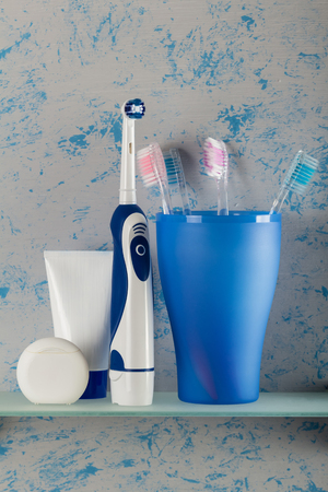Manual toothbrushes stand in a glass, next to an electric brush, on glass shelfの写真素材