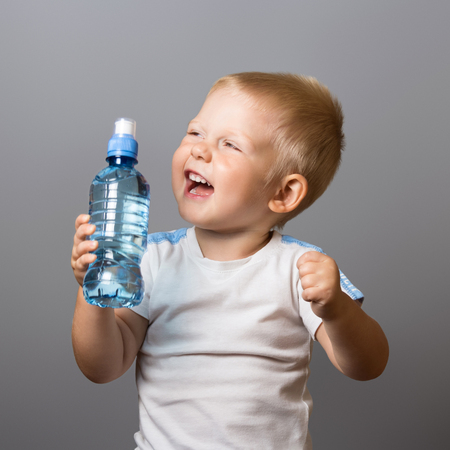 Laughing boy in white T-shirt with bottle of water, on gray backgroundの写真素材