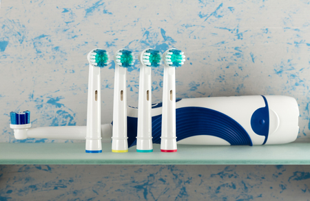 Electric toothbrush and replaceable nozzles of different colors, on glass shelfの写真素材