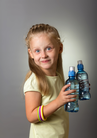 Charming girl holding two full bottles of water on gray backgroundの写真素材