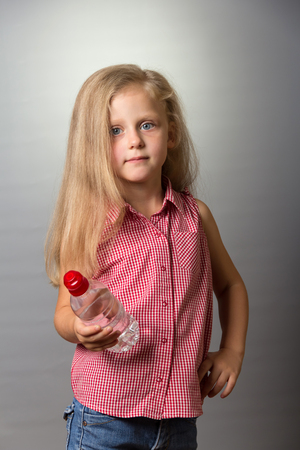Charming small girl with long hair holds bottle of water on gray backgroundの写真素材