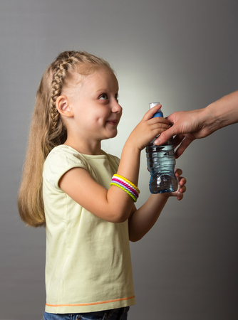 Little girl with beautiful hair takes from an adult a bottle of water, on gray backgroundの写真素材