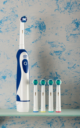 An electric toothbrush and multi-colored replaceable nozzles stand on glass shelfの写真素材