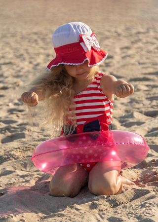 Blond charming girl in lifebuoy ring on the sandの写真素材