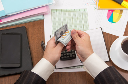 Office table with accessories, folders and documents, men's hands count moneyの写真素材