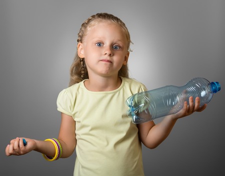Surprised little girl is standing with an empty bottle, on gray backgroundの写真素材