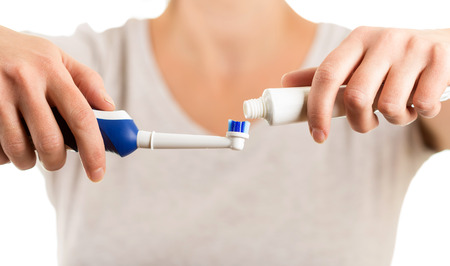 Female hands lay paste on electric toothbrush isolated on white backgroundの写真素材