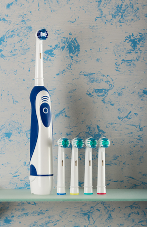 Electric toothbrush and replaceable nozzles of different colors on glass shelf,on blue backgroundの写真素材