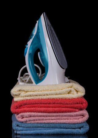 Modern electric iron stands on pile of terry towels, isolated on black backgroundの写真素材