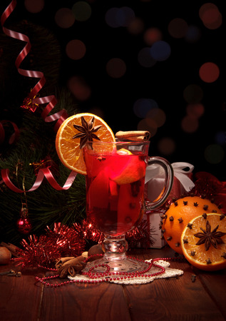 Spicy warming winter drink in glass, fruit and spices, New Year's tinsel, isolated on black backgroundの写真素材