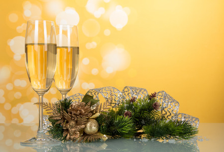 Two glasses with champagne, pine branch decorated with ribbon, New Year's souvenir on bright yellow backgroundの写真素材