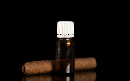 Bottle with liquid for smoking electronic cigarette, nearby cigar, isolated on black backgroundの写真素材