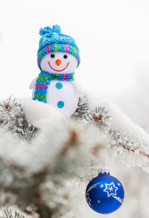 Little funny snowman and Christmas toy-ball, on snow-covered tree. Close-upの写真素材