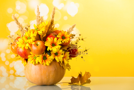 Original bouquet of apples, flowers and ears of corn in pumpkin, on bright yellow backgroundの写真素材