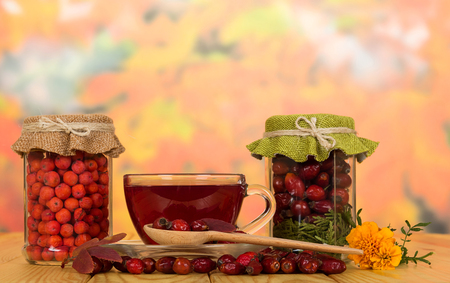 Banks with dry rosehip berries and mountain ash, cup of vitamin tea and saucer, on wooden tableの写真素材
