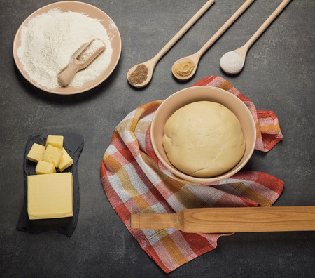 Finished dough in a bowl on a towel, flour and butter on grayの写真素材