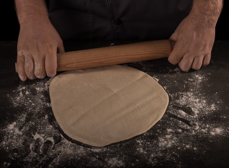 A layer of dough and rolling pin in the hands of Baker isolated on blackの写真素材