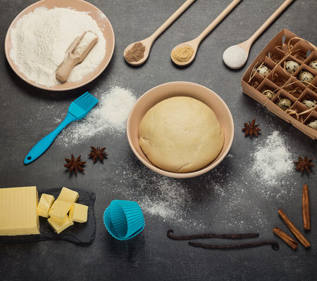 Finished dough in bowl, wooden spoons with spices, flour and butter on gray surfaceの写真素材