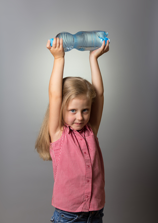 A little girl with long hair holds bottle of water from above, on grayの写真素材