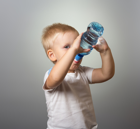 A little boy drinks water from bottle, on grayの写真素材