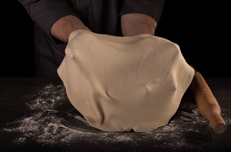 The rolled out layer of dough in the hands of Baker isolated on blackの写真素材