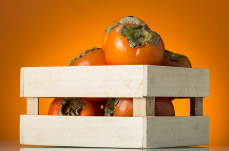 Wooden box full of ripe persimmon fruit on orange backgroundの写真素材