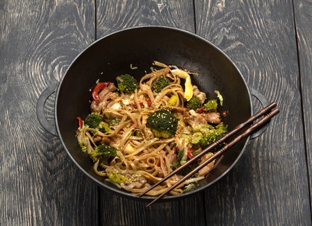 Asian dish of meat, vegetables and noodles with spices in wok, on background of tableの写真素材