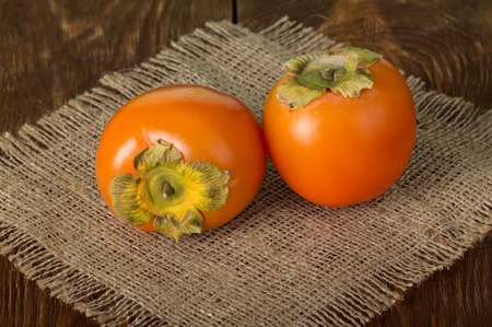 Two orange persimmons lying on wooden surfaceの写真素材