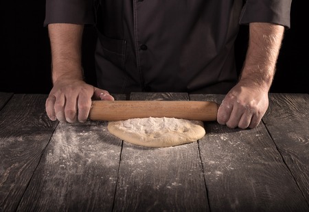 Confectioner forms layer of dough with rolling pin, isolated on black backgroundの写真素材
