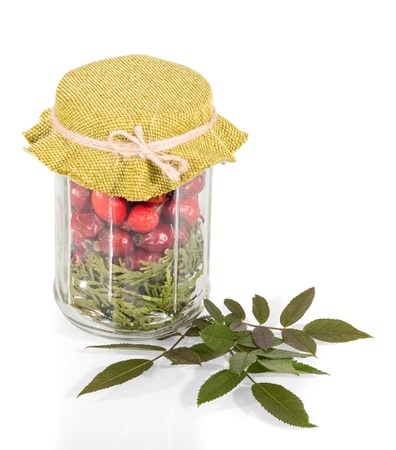 Glass jar with dry rose hip fruits, near green twig isolated on whiteの写真素材