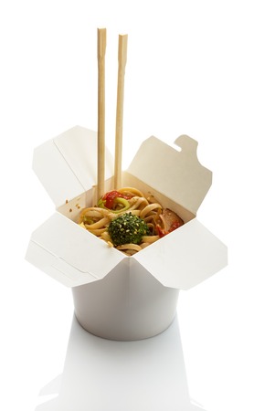 Spicy noodles with meat and vegetables in wok box, chopsticks isolated on whiteの写真素材