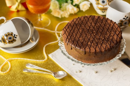 Festive table with chocolate cake on plate, tea set, spoons