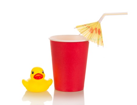 Plastic Cup with cocktail tubule and umbrella next to childs toy, isolated on whiteの写真素材