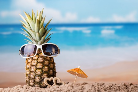 Pineapple with sunglasses near little hearts on the sandy beachの写真素材