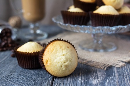 Lots of cakes in glass vase, in foreground two cupcakes in molds, on old tableの写真素材