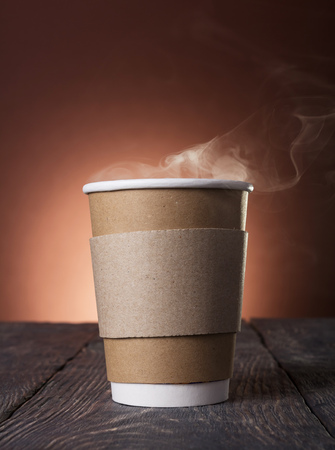 Disposable Cup of steaming hot coffee on wooden tableの写真素材