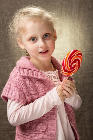 Little curly girl standing with candy in her handsの写真素材