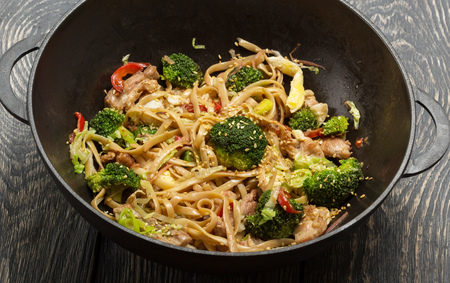 Spicy dish of noodles with meat and broccoli in frying pan-wok, on old surfaceの写真素材