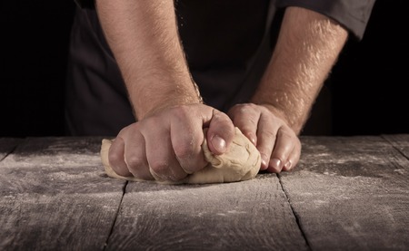 Bakers hands kneaded of dough on an wooden surface sprinkled with flour