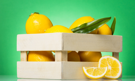 Lemons with leaves in wooden box, next to lemon wedges, on greenの写真素材