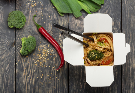 Hot fast food in box-wok, broccoli and chili pepper on wooden surfaceの写真素材