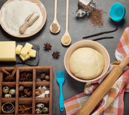 Dough in bowl, butter and other ingredients in box with cells, on gray backgroundの写真素材