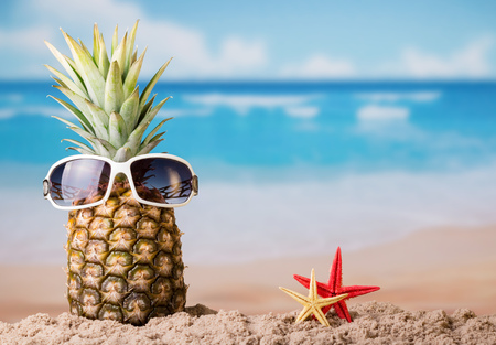 Funny pineapple with glasses and two starfish, on sandy beachの写真素材