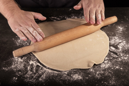 Thin layer of dough, rolling pin in Baker's hands, isolated on black backgroundの写真素材